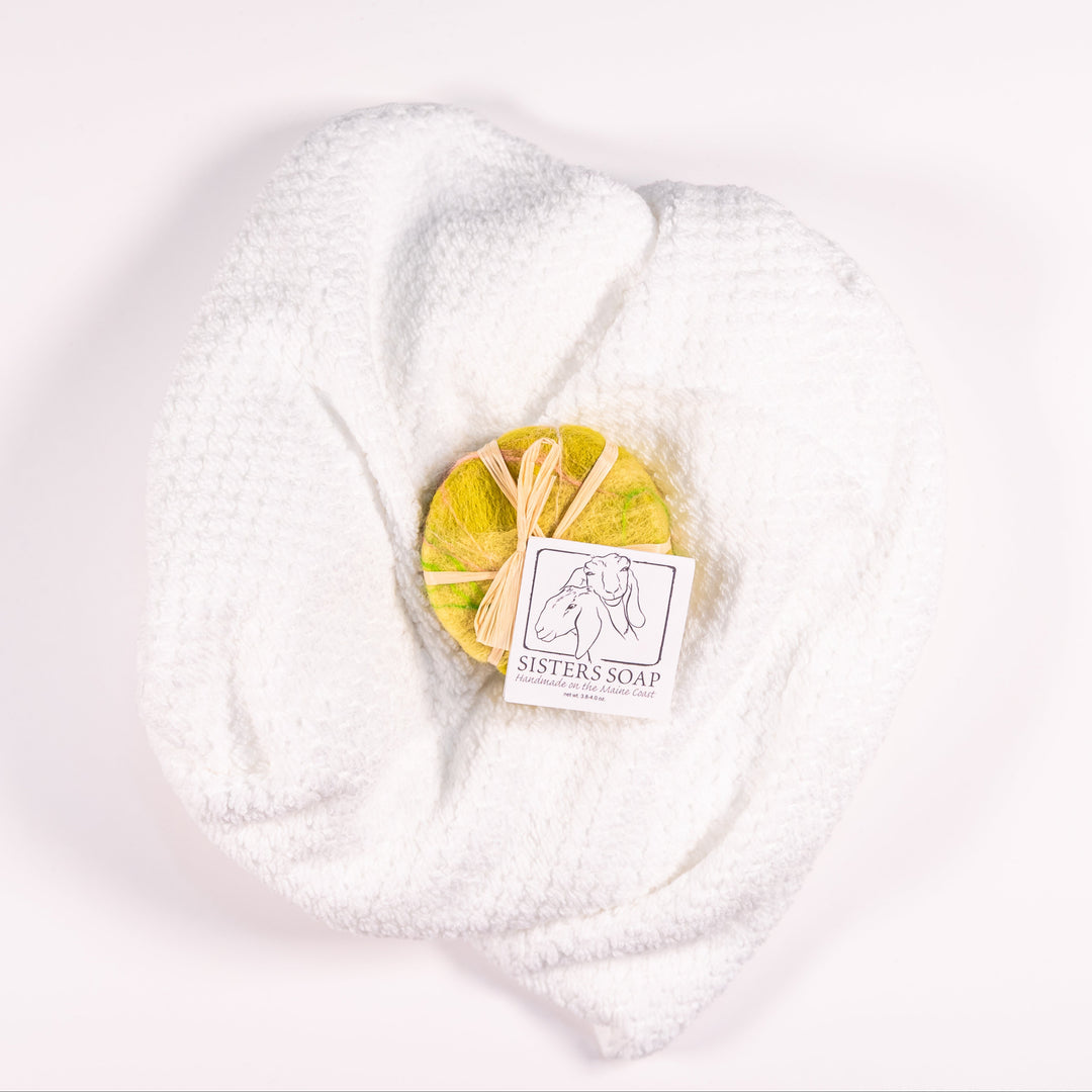 A round bar of soap covered in felt, resting on top of a white towel