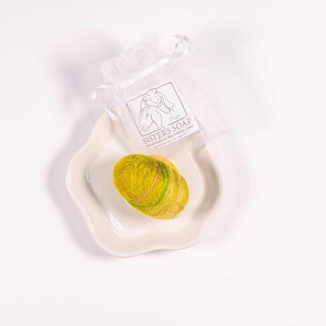 An egg-shaped soap covered in felt, resting in a white dish