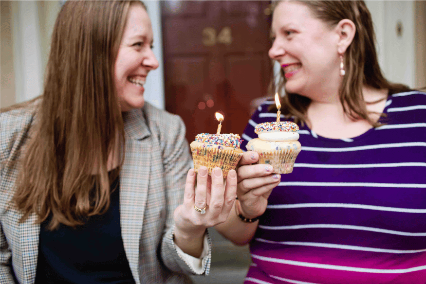 Two sisters hold two cupcakes with lit candles on top