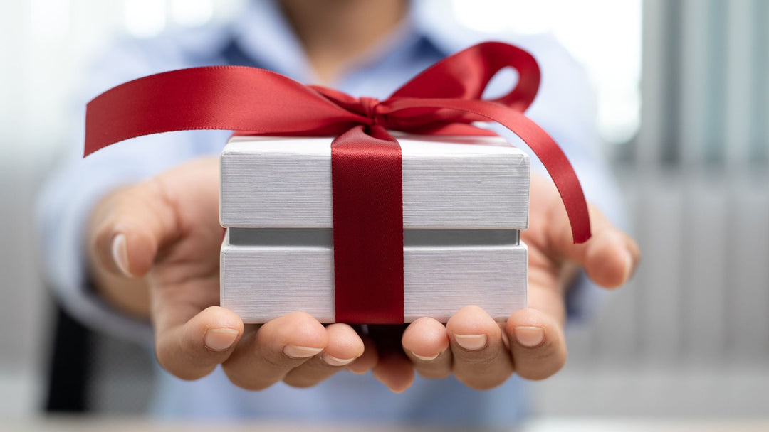 two hands holding out a small white gift with a red ribbon