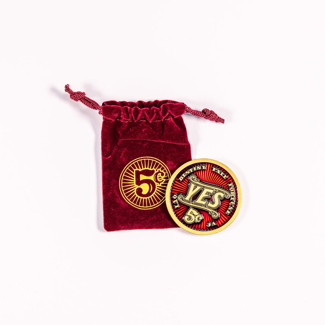 A 2-inch metal coin sitting on top of a velvet red bag