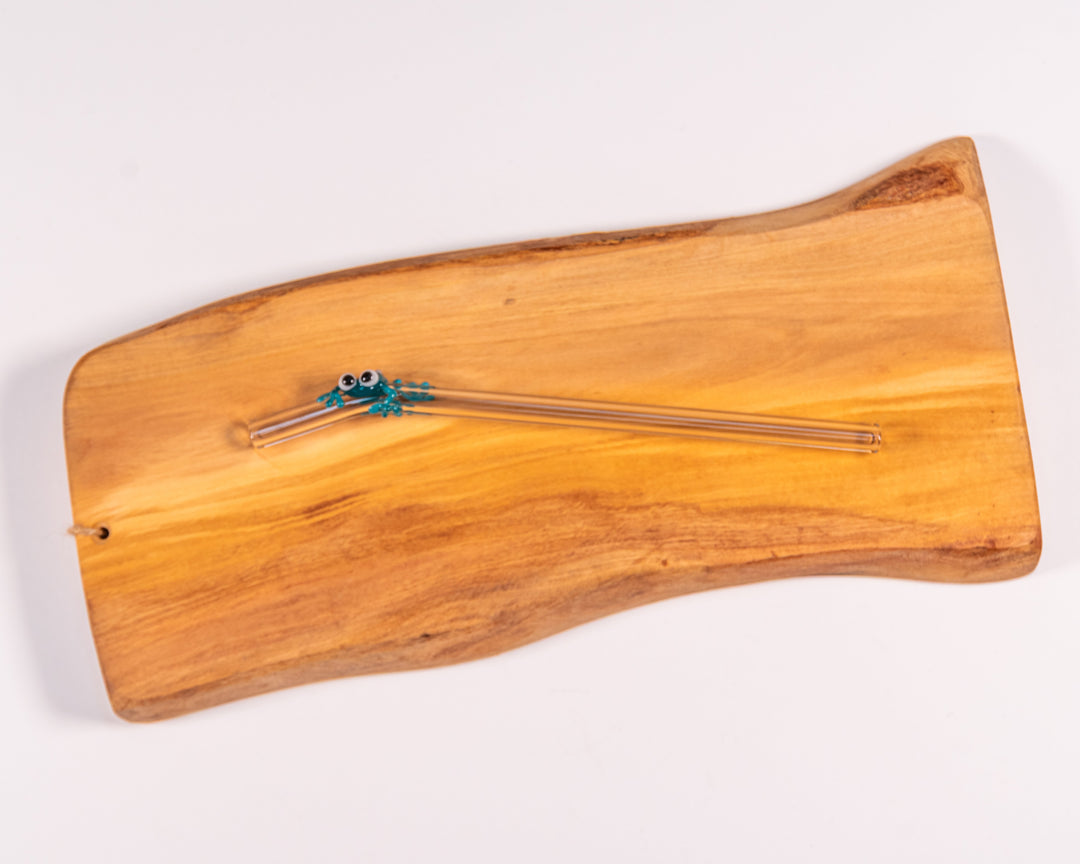 A glass straw featuring a glass-blown green frog, resting atop a background of wood