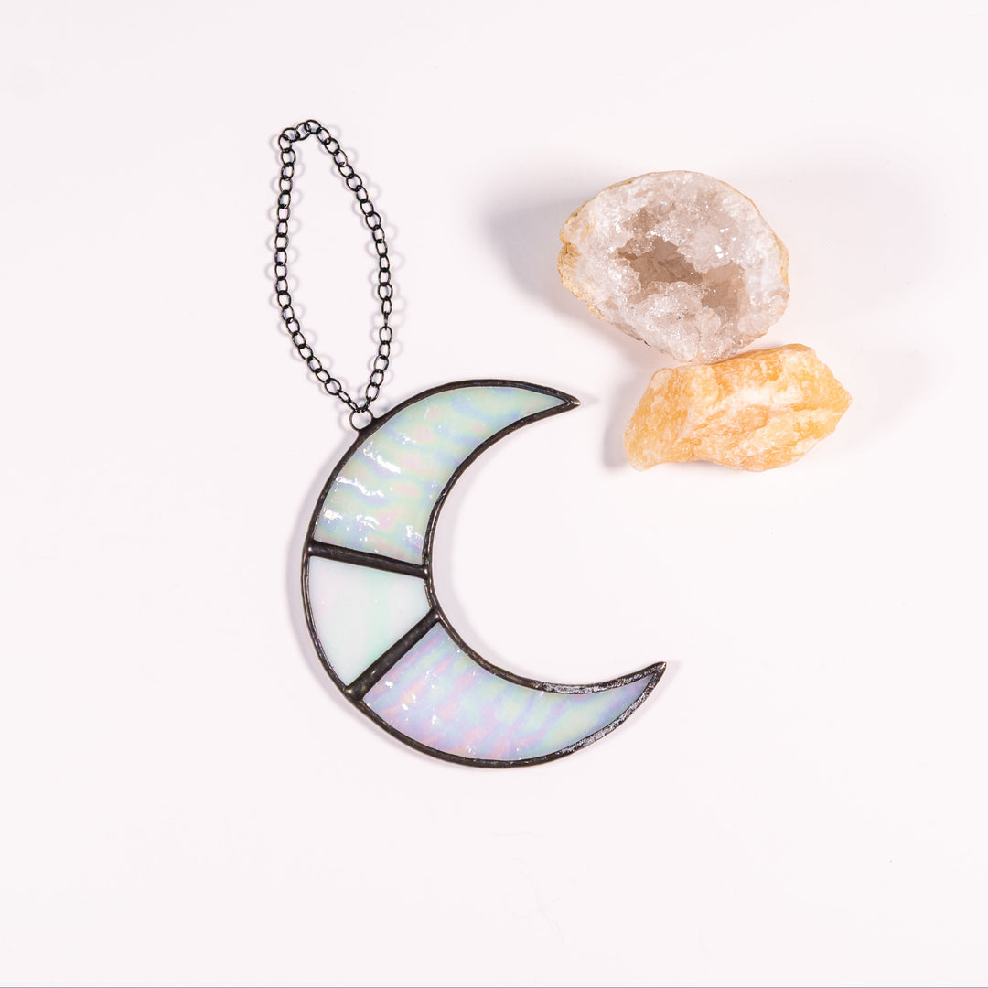 An iridescent stained-glass moon pendant on a short chain on a white background