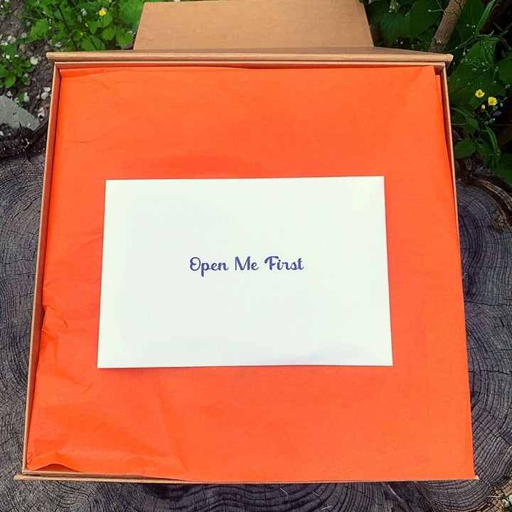 'Open me first' envelope sitting on top of orange tissue paper in open Countdown Calendar